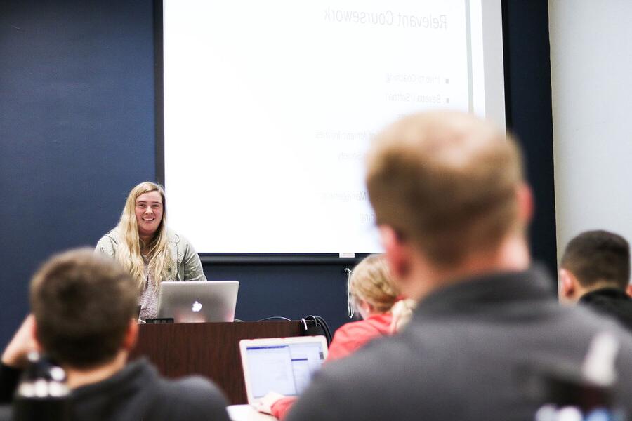 Young woman at a podium smiling in front of a class